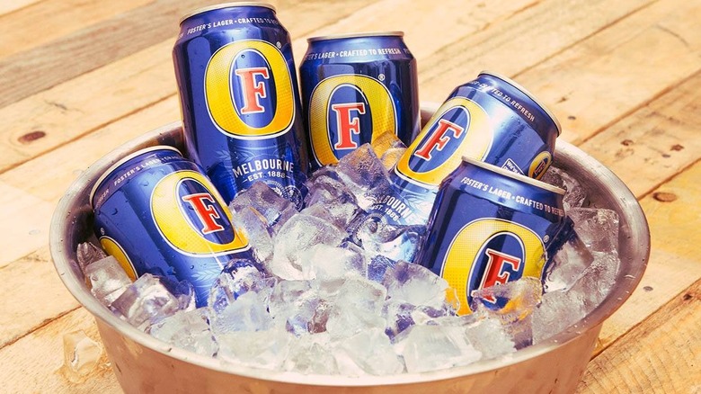 A collection of Foster's cans in an ice bucket placed on wooden decking