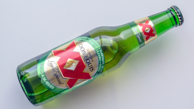 A top-down shot of a bottle of Dos Equis Especial laid diagonally on a plain background
