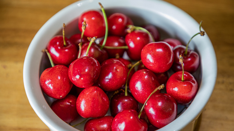 white bowl full of red cherries with green stems