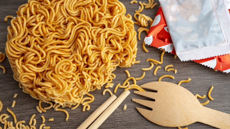 Dry instant ramen on a dark wooden surface with chopsticks, a wooden spork, and sauce packets