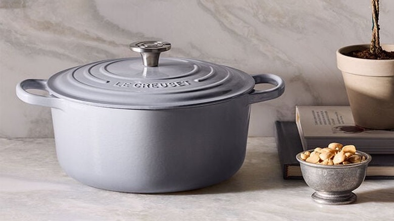 A 5.5-quart Le Creuset Signature Round Dutch Oven in Chateaux on a marble countertop next to a small silver bowl of nuts.