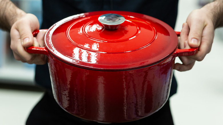 red Dutch oven with a lid on being held by someone