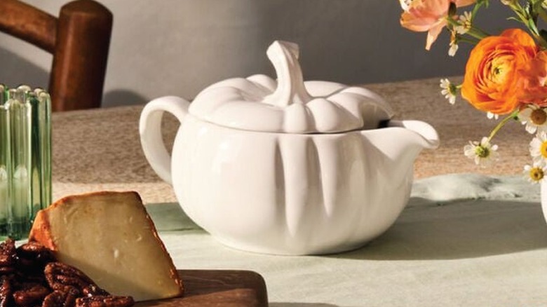 Le Creuset's Pumpkin Gravy Boat in white with a board of cheese and candied nuts on the same table with orange flowers and daisies.