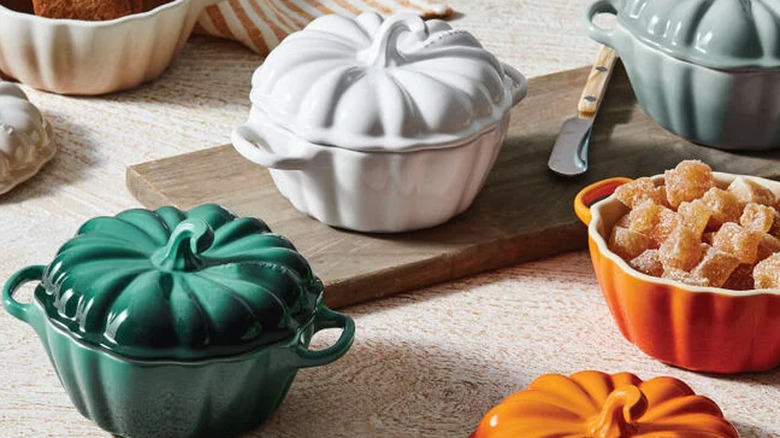 Four Pumpkin Mini Cocottes in white, persimmon, seasalt, and foret around a cutting board.