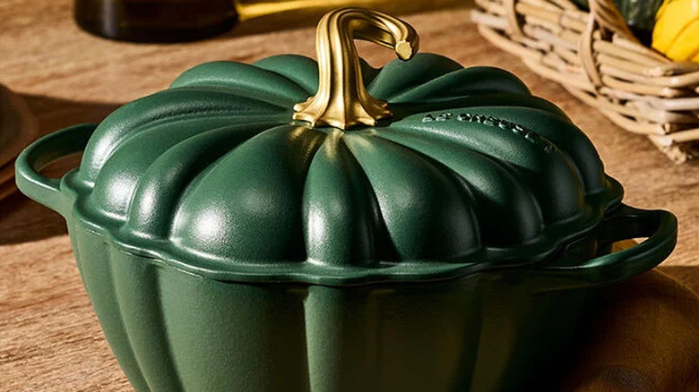 The Signature Pumpkin Cocotte in Foret on a table with a basket of squash in the background.