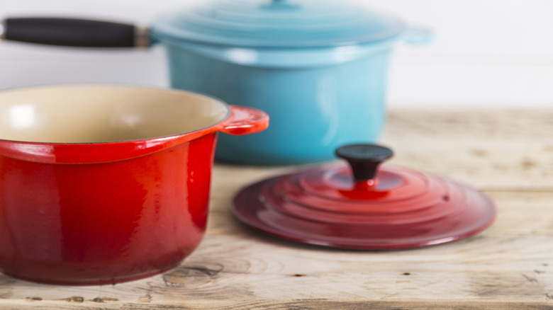 Red and blue Le Creuset cookware with lids on wooden table