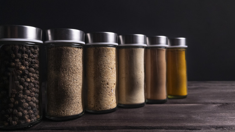 Six glass spice jars with aluminum lids, lined up on a wooden table
