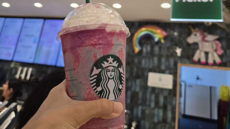 A hand holding a Unicorn Frappuccino from Starbucks