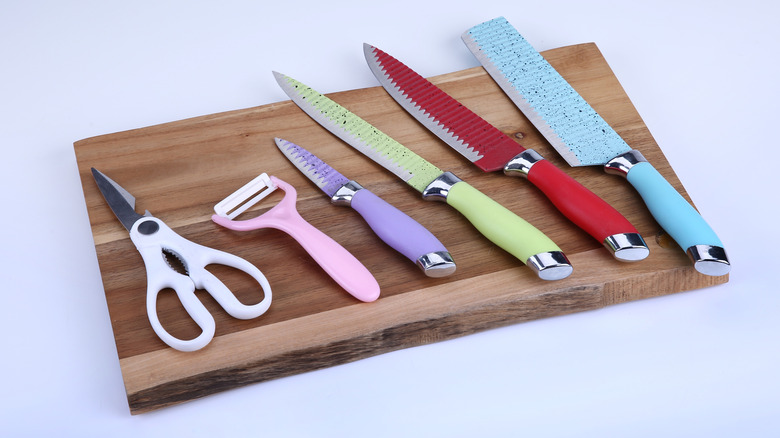 Row of kitchen scissors and knives on cutting board