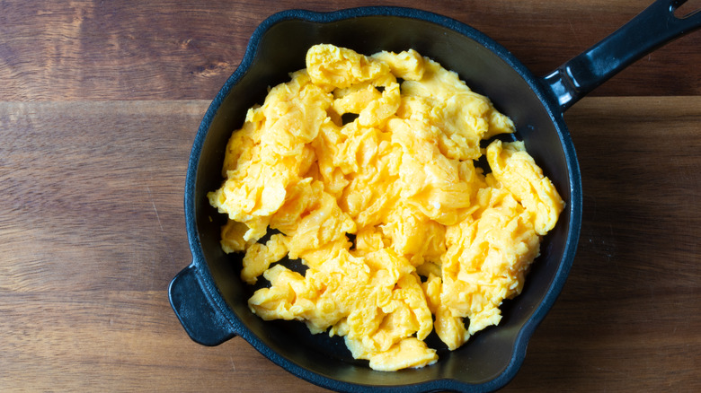 A black skillet full of scrambled eggs on a wooden table top