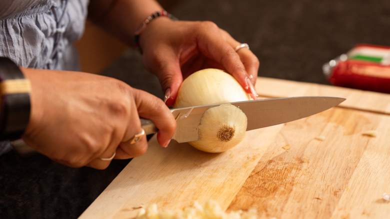 Close-up of the hands of a woman using knife to cut onion on chopping board