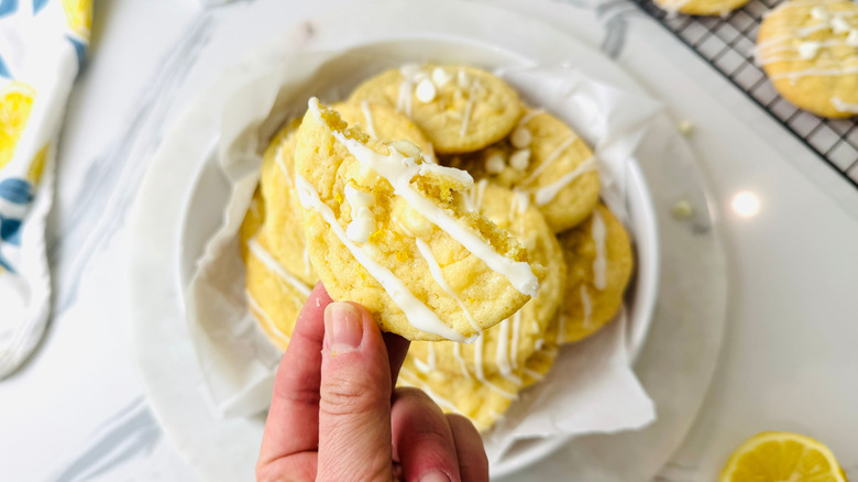 Hand holding lemon white chocolate chip cookie above bowl of cookies