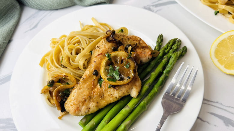 Sheet pan chicken piccata on plate with pasta and asparagus