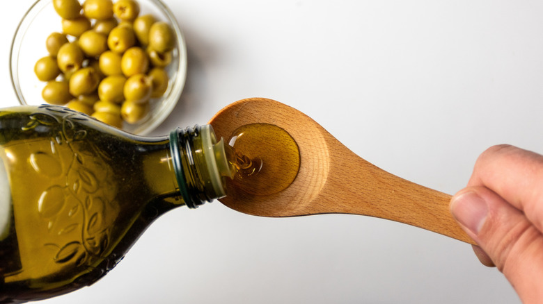 Extra virgin olive oil being poured into a wooden spoon, with bowl of olives in the background