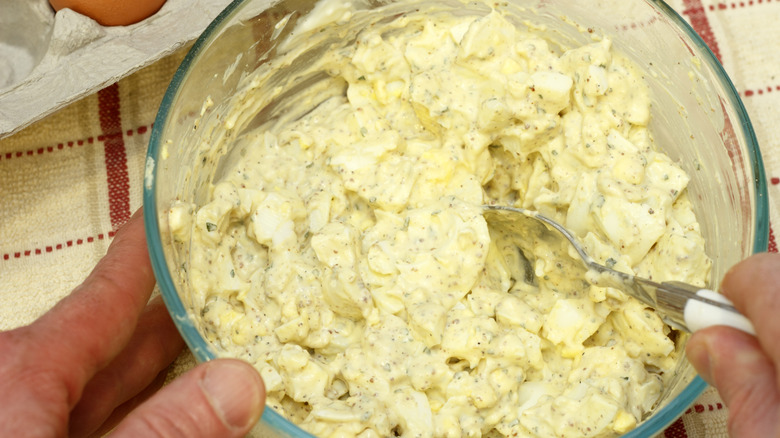 Hand mixing egg salad in a bowl