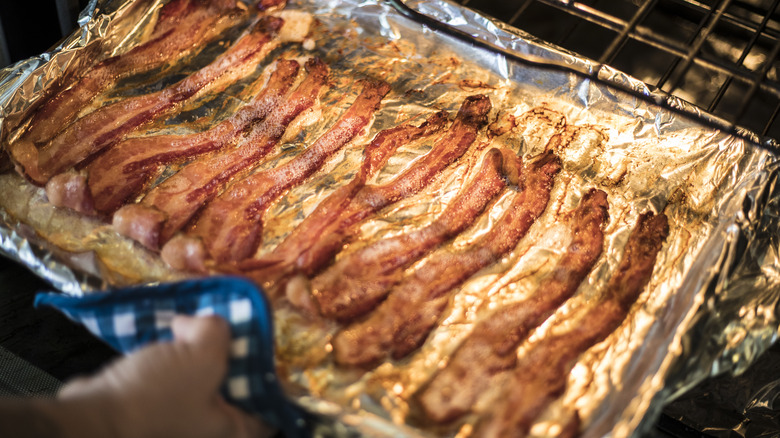 Hand pulls out bacon on foil from oven 