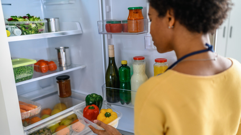 Woman holding peppers by open fridge