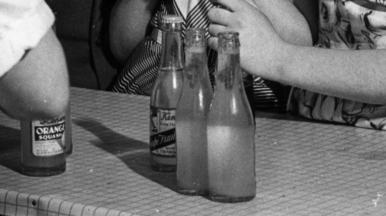 A black and white vintage image of some light soda bottles on a busy counter.