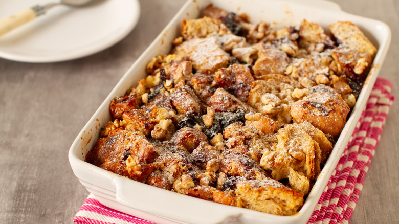 A white baking dish containing sweet bread pudding, dusted with powdered sugar