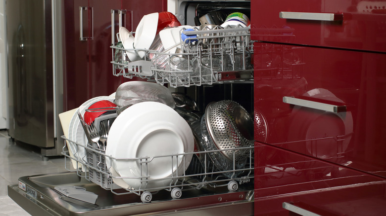 A fully-loaded dishwasher with the racks extended, next to red cupboards