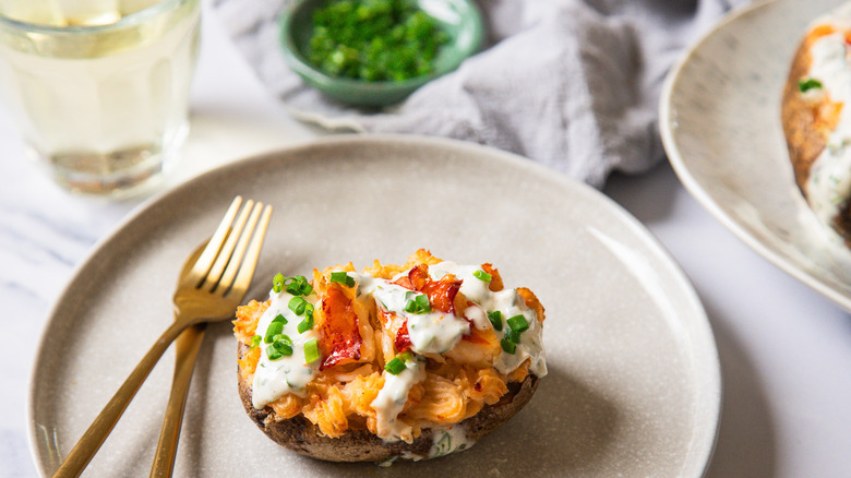 Lobster-stuffed baked potato on a plate with cutlery besides a glass of wine.