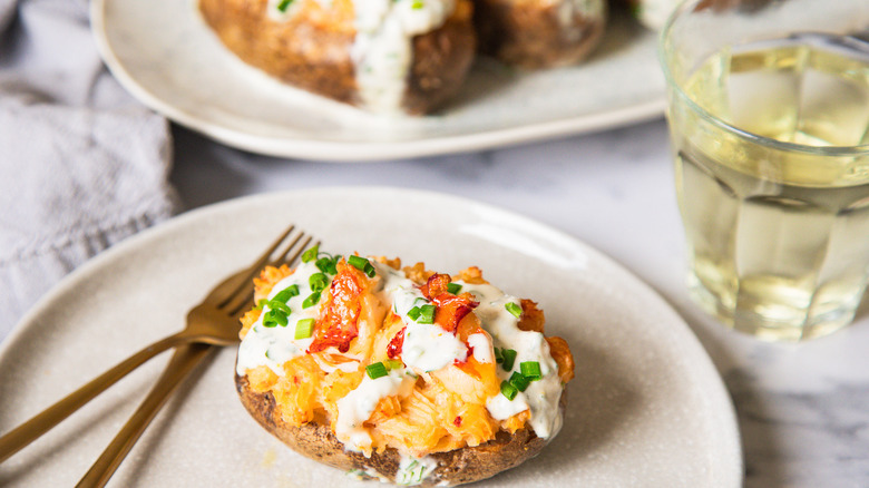 Lobster-stuffed baked potato on a plate with cutlery besides a glass of wine.