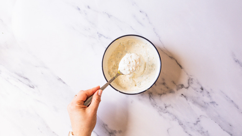 Hand lifting a spoon of herb sauce from bowl.