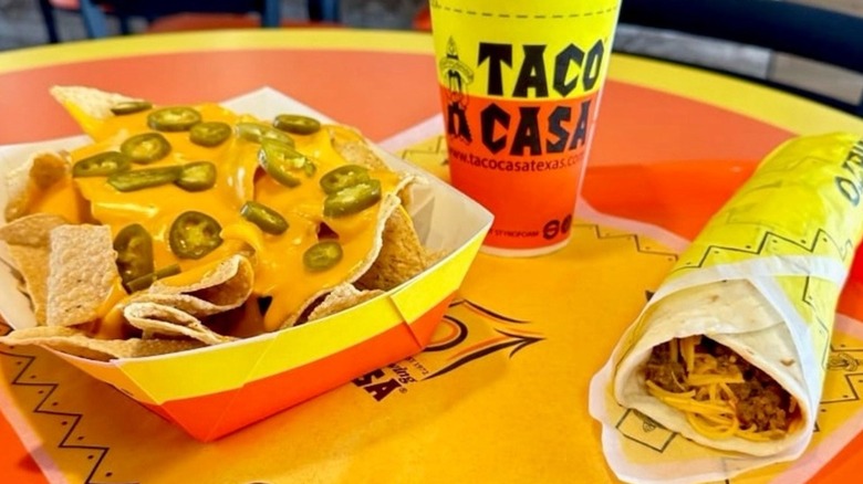 Nachos, a burrito, and a drink from Taco Casa sit on a table.