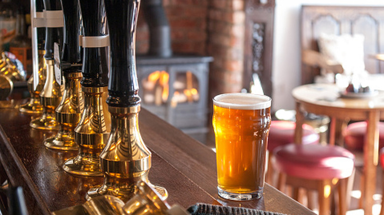 a pint of lager on the bar next to the draught handles at a traditional pub