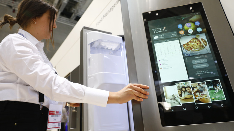 Sales associate displays modern smart fridge with screen