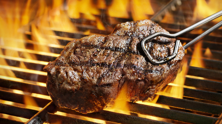 A person uses tongs to grill steak