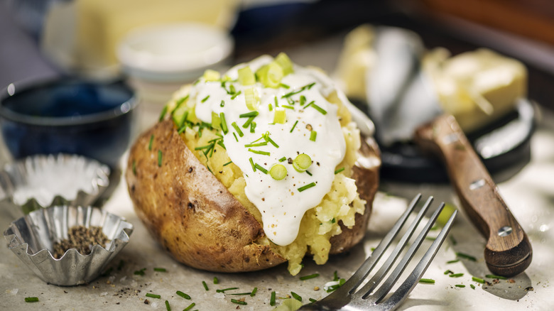 baked potato with sour cream and chives with knife and fork