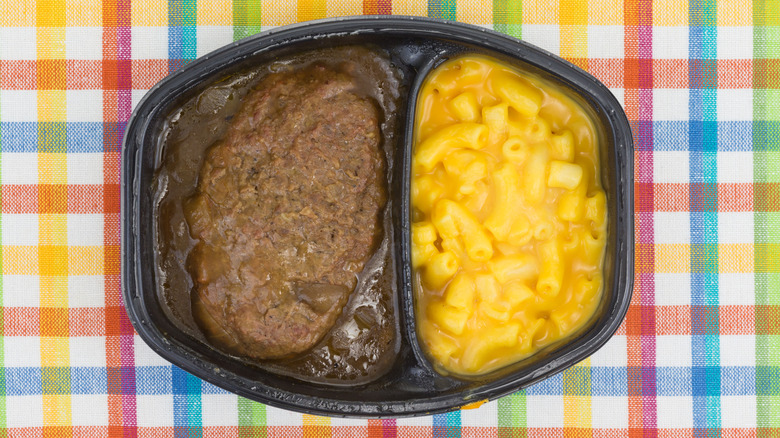 Frozen TV dinner tray with Salisbury steak and macaroni and cheese on a colorful tablecloth