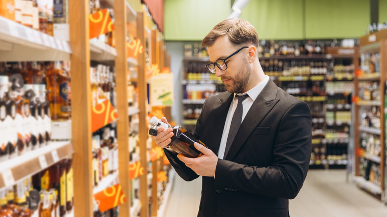 A man reads a whiskey bottle in a liquor store.