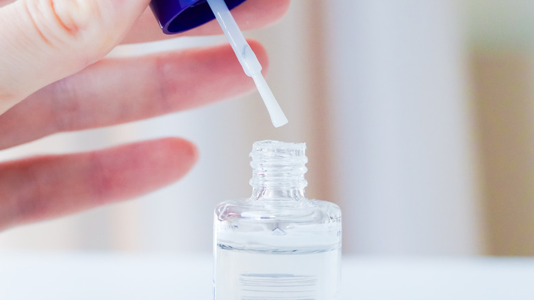 Hand lifting brush out of clear nail polish bottle