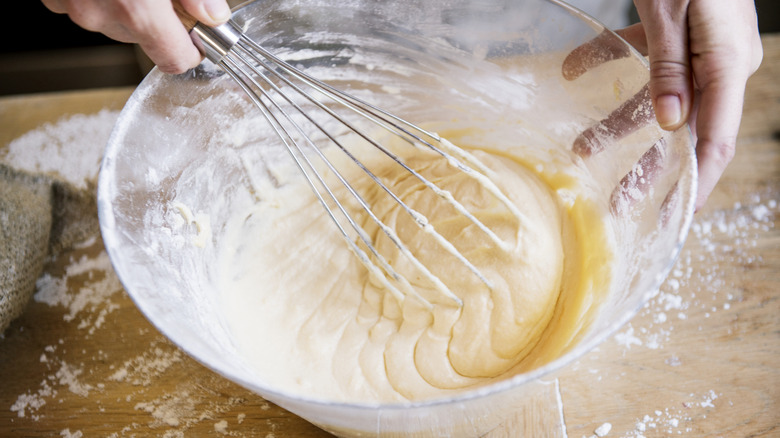 a person whisking cake batter in a glass bowl