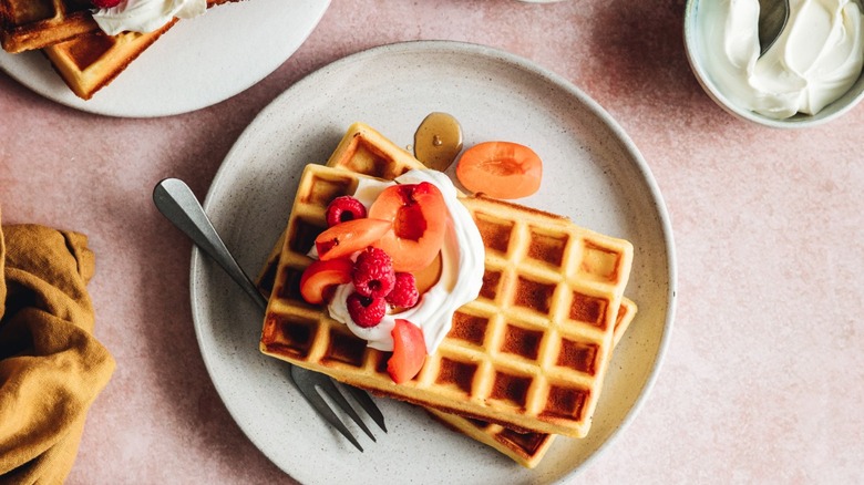 plate of waffles with cream, syrup, and berries
