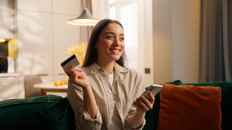 Person smiling while holding a phone and a credit card