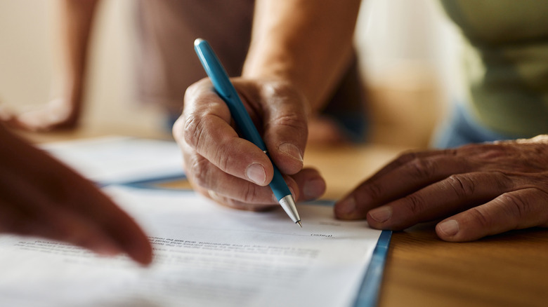Hand signing paperwork with a pen on a wooden tabletop