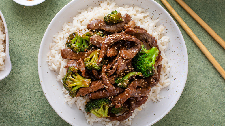Beef and broccoli stir fry served over rice on white plate on green table