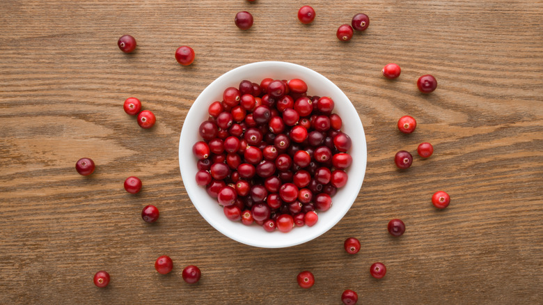 Full white bowl with fresh red cranberries on dark brown wooden table