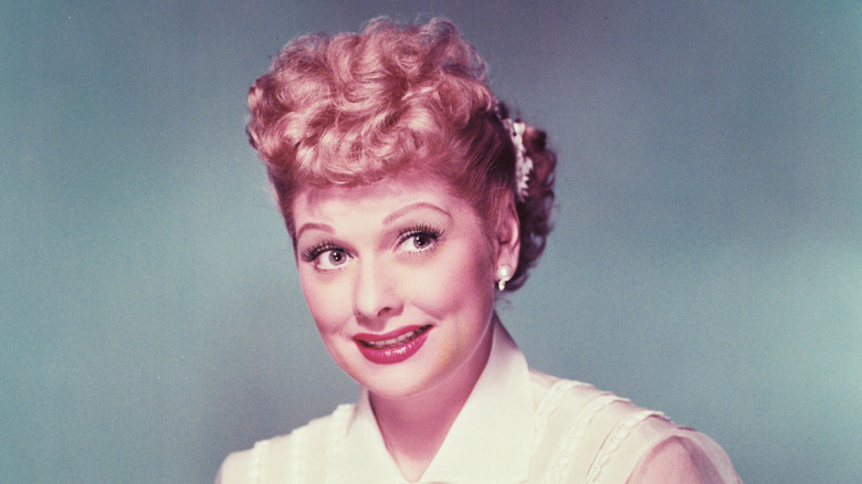 Lucille Ball wearing a white blouse with white chiffon sleeves in a studio portrait, against a grey background, circa 1955