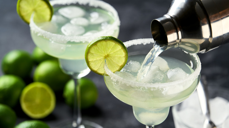 Margarita cocktail is poured from a shaker into a glass with a slice of lime and an edge of salt along the edge