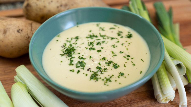 Close up of cold Vichyssoise soup in blue bowl surrounded by leeks and potatoes