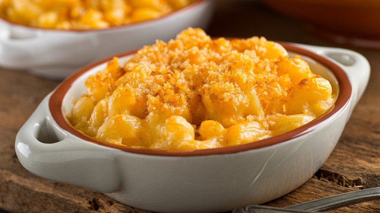 Baking dish of macaroni and cheese on a cutting board with a spoon.
