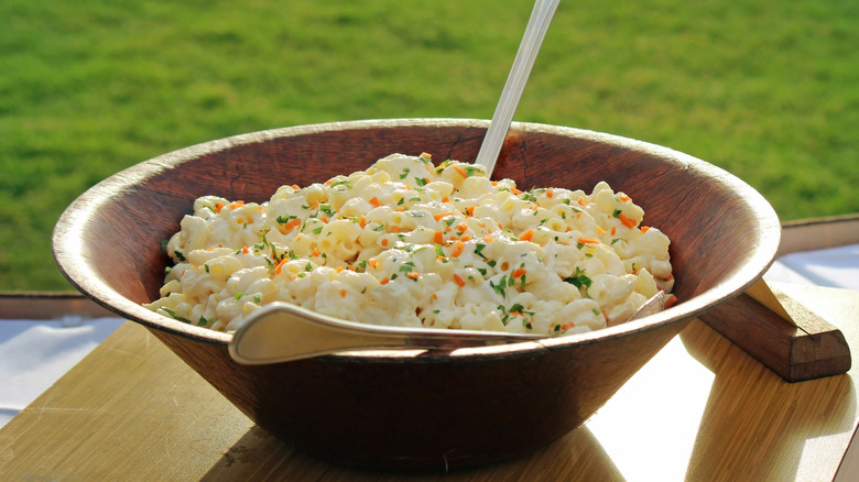 A wooden bowl of Hawaiian-style macaroni salad on an outdoor table with grass in the background
