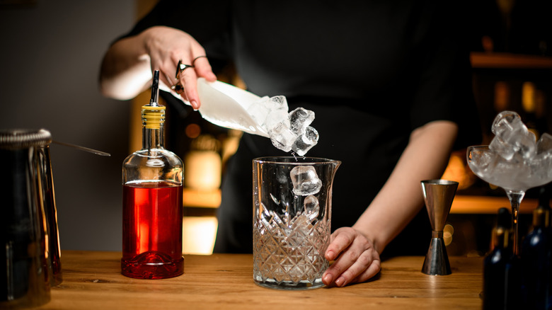 Adding ice to cocktail glass alongside rum and tools