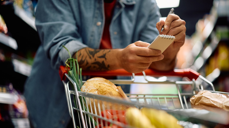 Person leaning on shopping cart while looking at grocery list