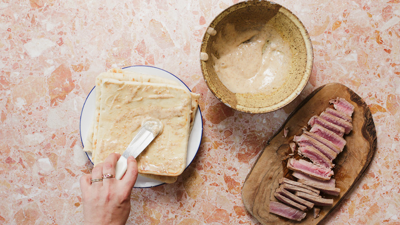Spreading flatbreads with mayo next to plate of tuna