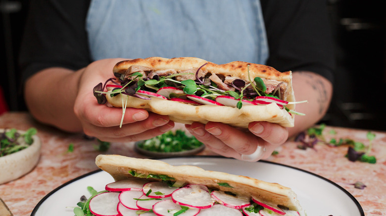 Hands holding ahi tuna flatbread above ahi tuna flatbread on plate